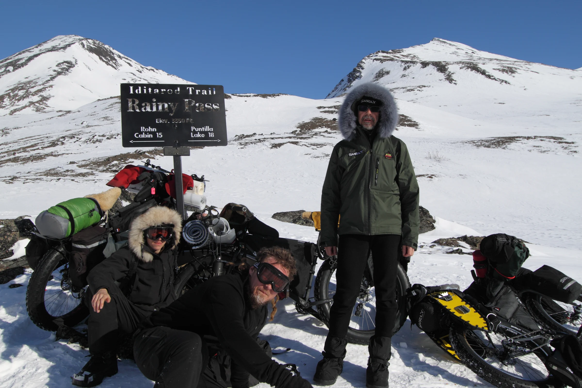 Travellers beside the Iditarod Trail summit sign at Rainy Pass in the Alaska Range